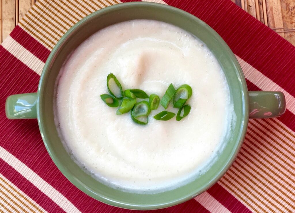 Goat cheese cauliflower soup on a tan and red placemat in a green bowl