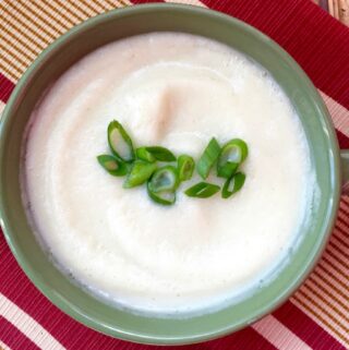 Goat cheese cauliflower soup on a tan and red placemat in a green bowl