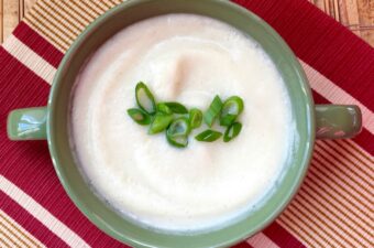 Goat cheese cauliflower soup on a tan and red placemat in a green bowl